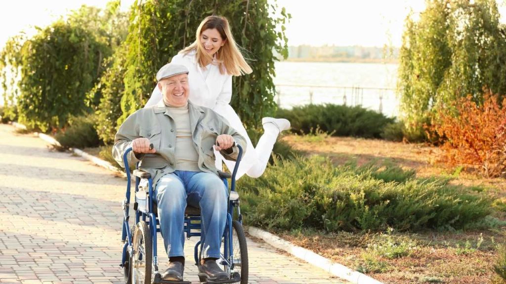 young effervescent caregiver pushing their patient in a wheelchair both laughing